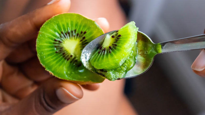 Person holding spoon digging into a kiwi