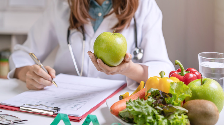 Woman in white lab coat holding fruit and taking notes