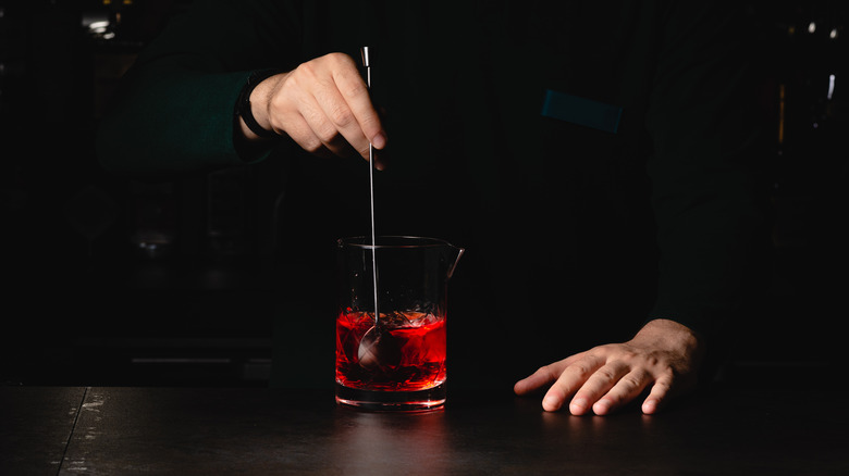 Hand using stirring spoon to make a negroni