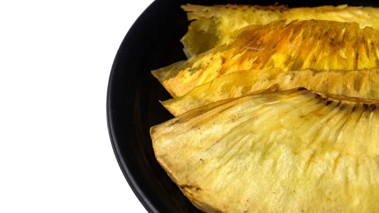 Black plate holding four pieces of fried breadfruit with white background