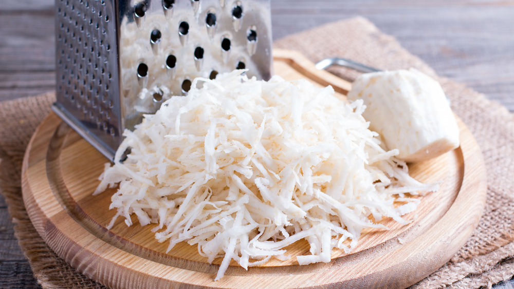 Grated celeriac on a wooden cutting board with box grater