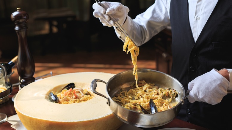 Person putting seafood pasta in cheese wheel