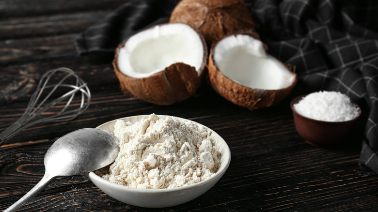 Coconut flour in bowl with spoon next to coconuts