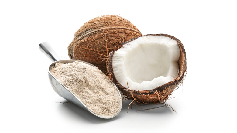 Metal scoop with coconut flour next to raw coconut