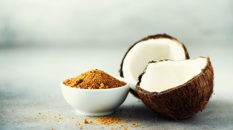 Bowl of coconut sugar next to halved coconut fruit 