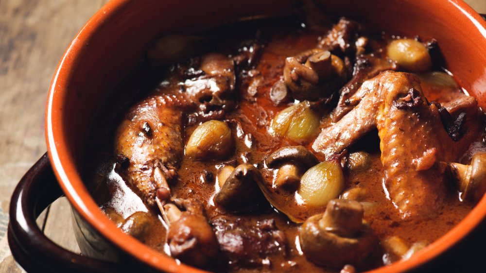Coq au vin: Chicken leg and wing with dark red sauce in a red stock pot.