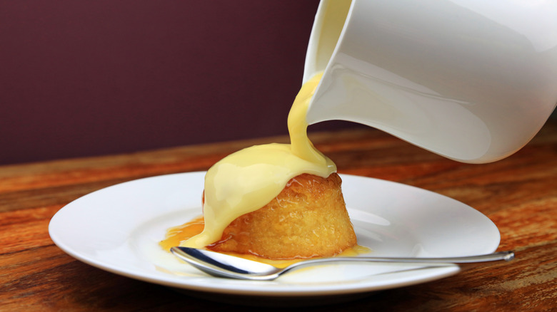 Pouring custard from a white pitcher onto bread pudding