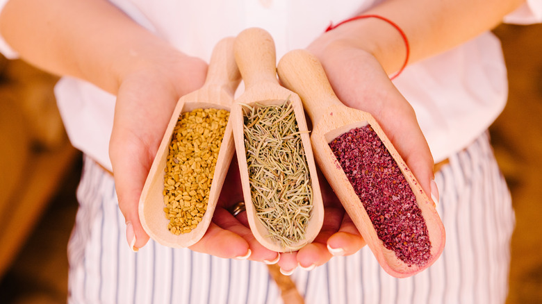 person holding three wooden spoons with spices