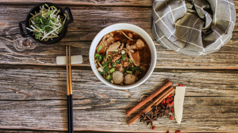 Bowl of soup and various ingredients on wooden surface