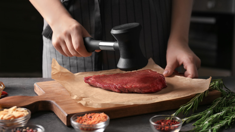 Chef using meat mallet on steak