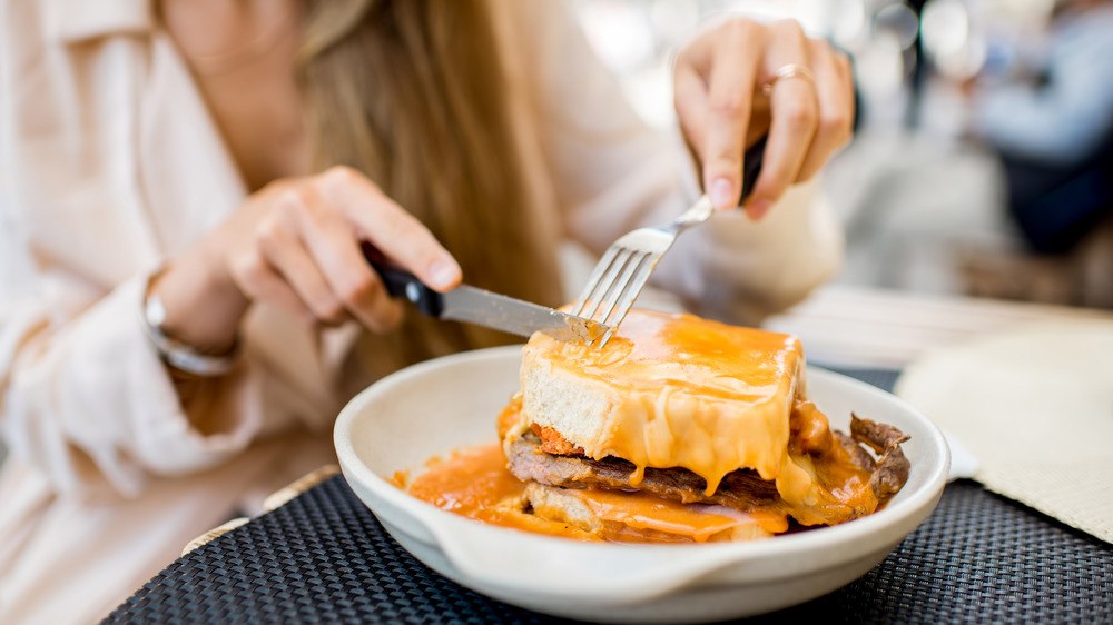 Woman cutting juicy Francesinha sandwich