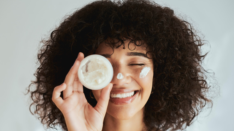 Person smiling and holding up tub of moisturizer