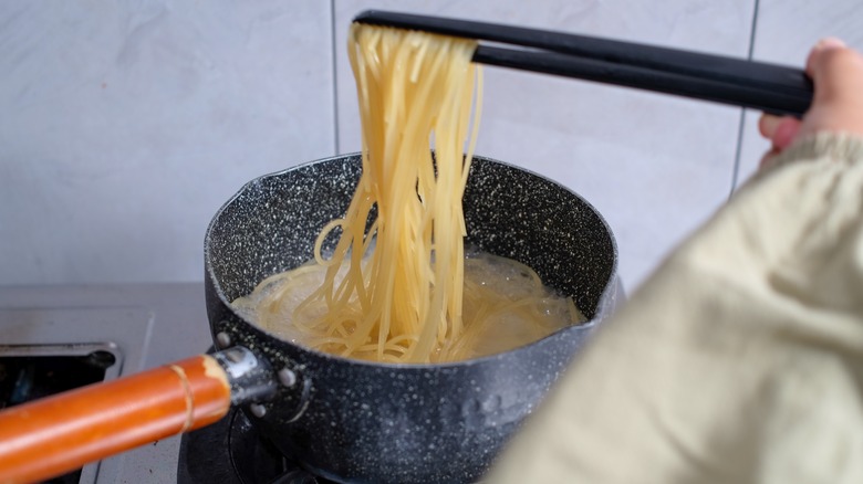 Spaghetti being lifted from pan with tongs