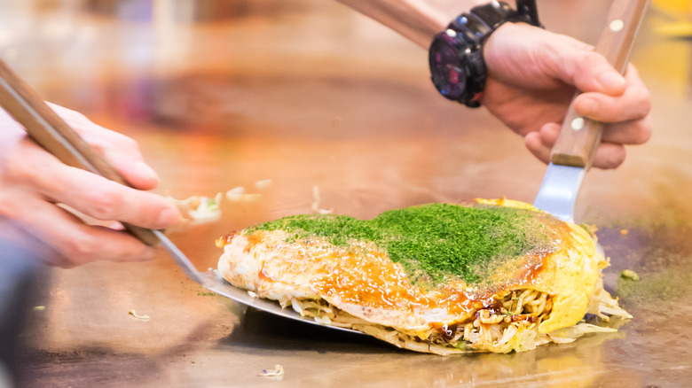 Okonomiyaki being lifted from griddle