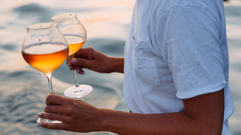 Person holding glasses of orange wine