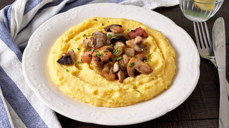 Polenta in white dish with mushrooms next to utensils