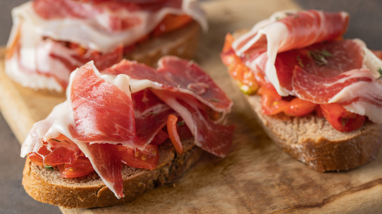 Thin slices of prosciutto on top of bread and tomatoes