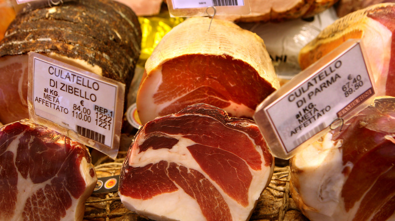 Italian ham varieties with tags at a deli market.