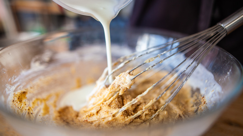 Pouring milk into batter in a glass bowl with a whisk