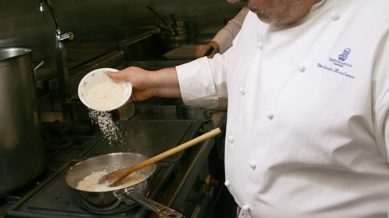 Chef pours cheese into a pan of risotto to finish 