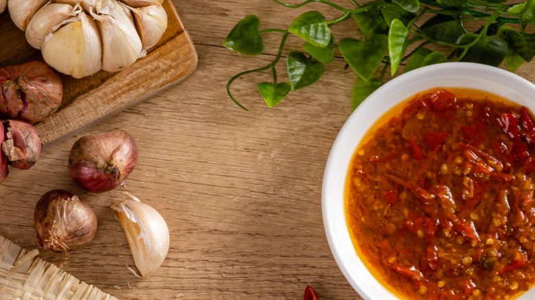 White bowl with sambal belacan beside garlic cloves on wooden background