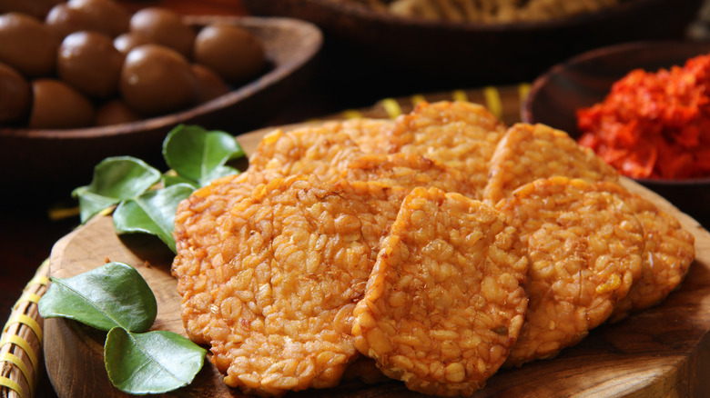 Slices of cooked, marinated tempeh next to leaves