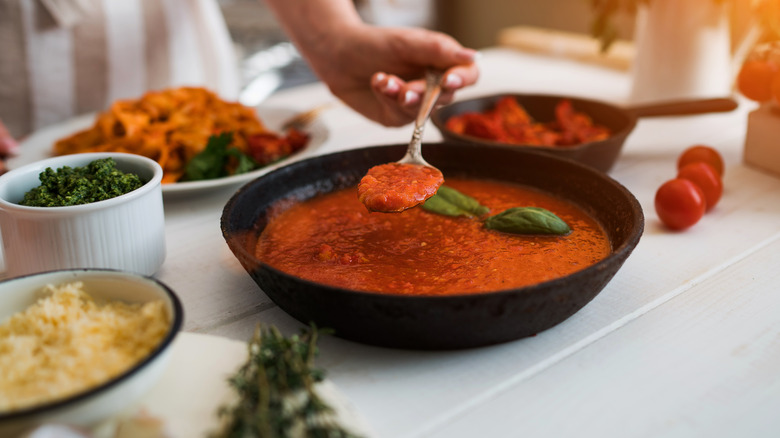 A hand holding up a spoonful of tomato sauce