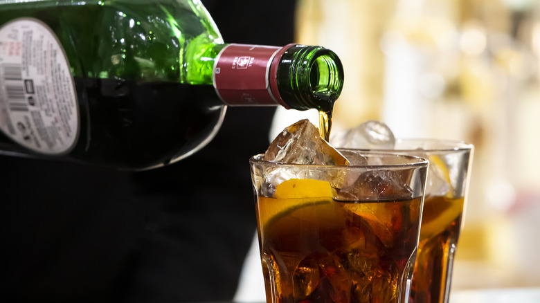 Server pouring vermouth into a rocks glass over ice