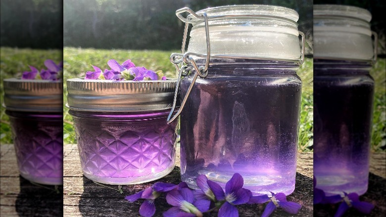 one jar of violet syrup, another glass jar filled with violet petals