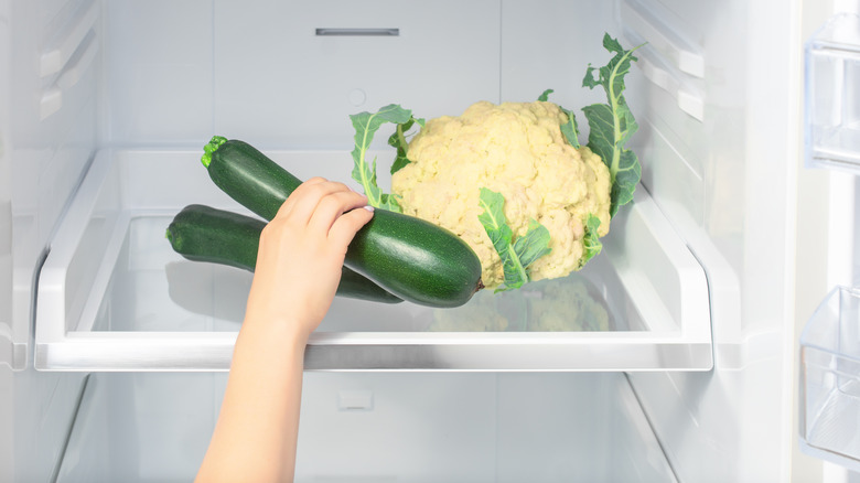 Hand taking zucchini from a fridge 