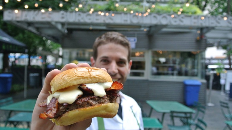 Culinary Director holding a Shake Shack burger in front of Madison Square Park