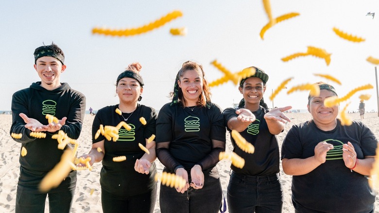 Five Shake Shack employees throwing out crinkle cut fries to the camera