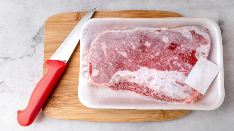 packaged frozen steak on cutting board with knife