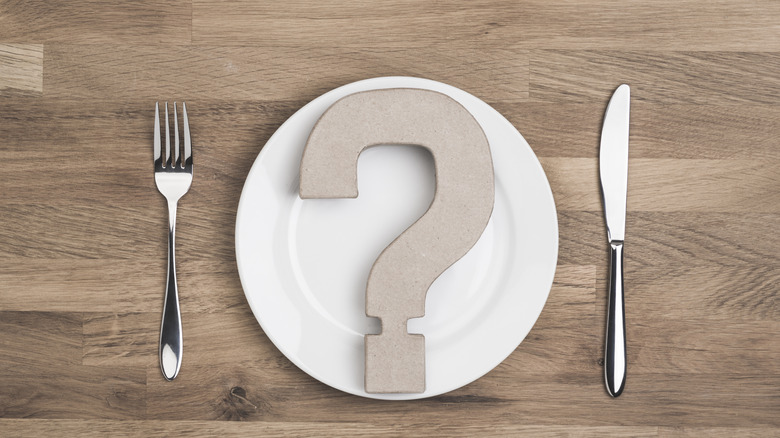 Wooden question mark on white plate with utensils