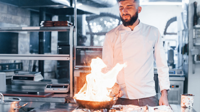 a cook looking at a frying pan on fire