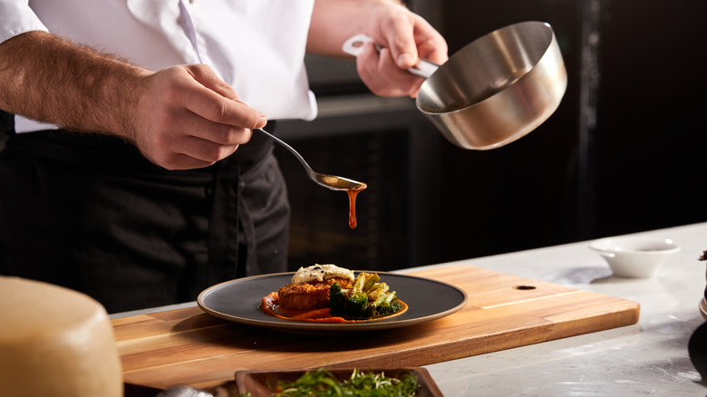 A chef spooning sauce onto a dish