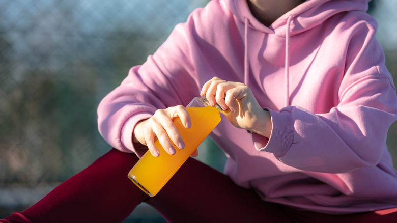 Person in pink sweatshirt holding orange sports drink