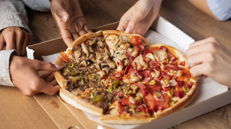 Hands grabbing slices of pizza from a pizza pie