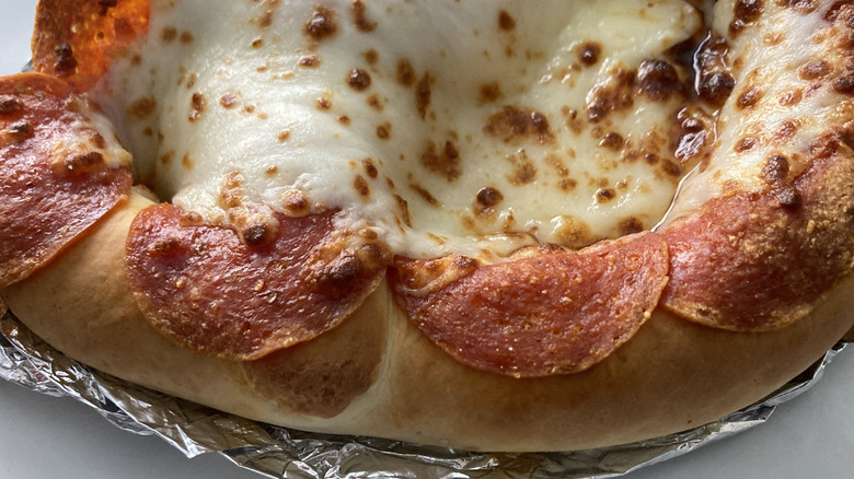 A closeup shows the pepperoni slices hanging over the edge of the crust.