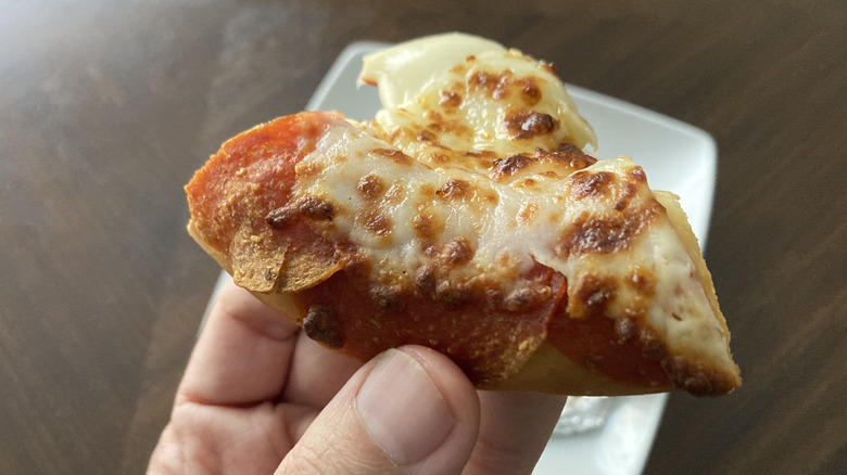 A slice of pepperoni pizza pretzel is being held by hand.