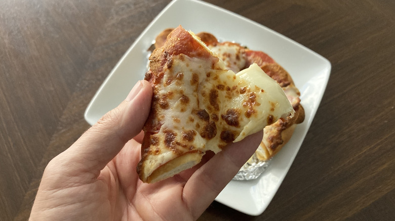 A hand holds a triangle-shaped bite of the pizza pretzel.