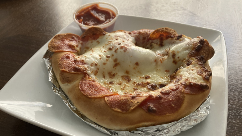 A pizza pretzel sits next to sauce on a plate.