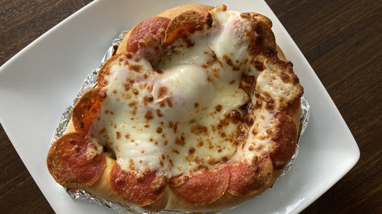 A pizza pretzel is topped with cheese and pepperoni.