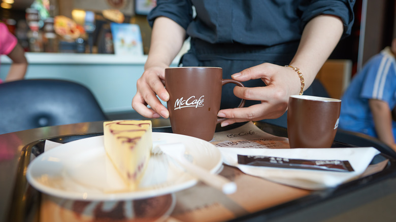 A McCafe employee holding a cup of coffee with a cheesecake in the forefront