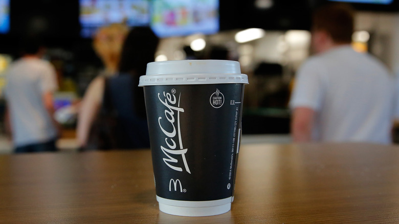 A black McCafe cup sits alone in the foreground while McDonalds is busy in the background