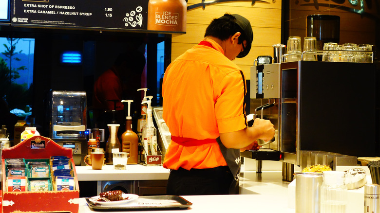 A McCafe employee making coffee, syrups in the background