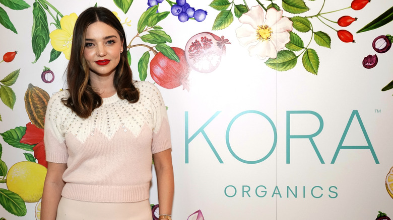 Miranda Kerr in front of a Kora Organics backdrop with fruits and vegetables