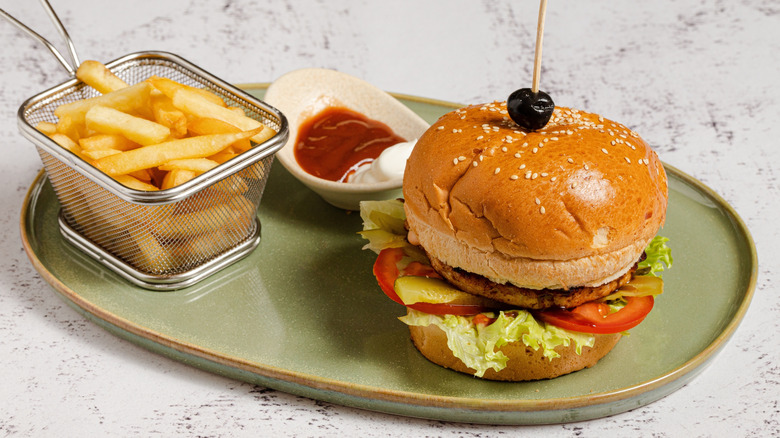 green plate of grilled chicken sandwich, basket of french fries, and side of ketchup and mayo