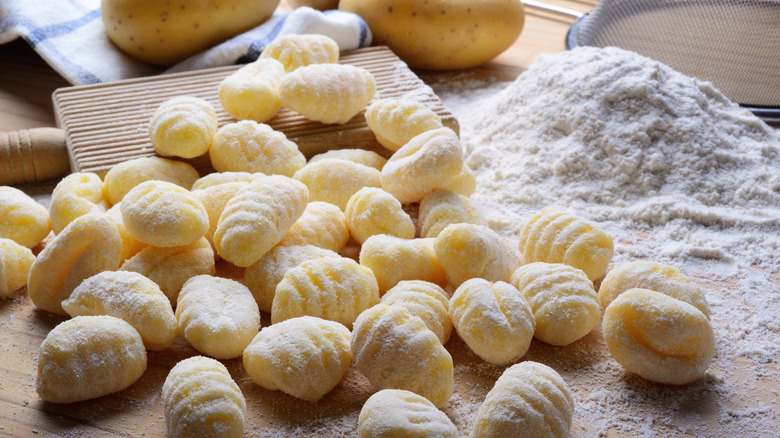 Fresh gnocchi and pile of flour on wooden table