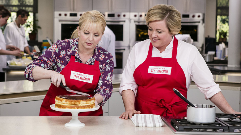 Two America's Test Kitchen cast members frosting a cake